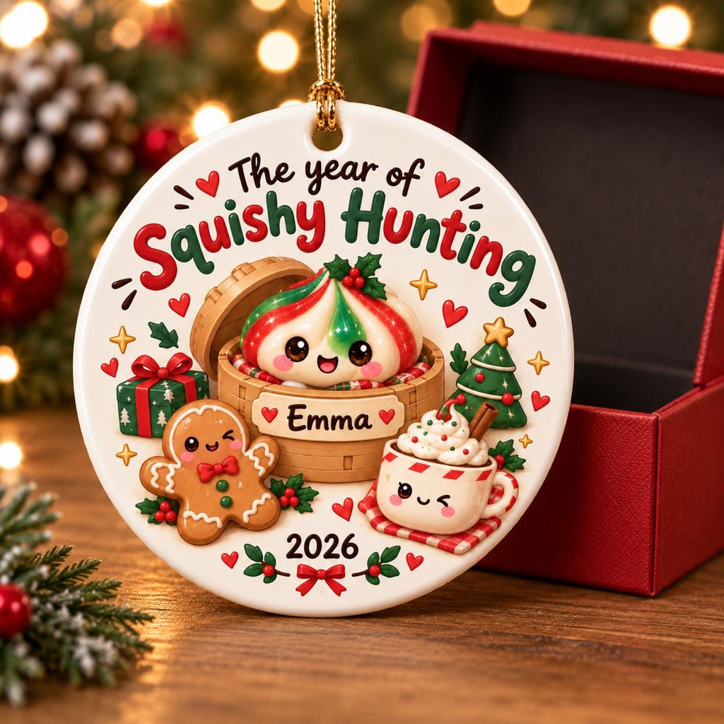 May include: A round white ceramic Christmas ornament featuring the text The year of Squishy Hunting and 2026. The design includes a cute dumpling in a bamboo steamer labeled Emma, a gingerbread cookie, a gift box, a Christmas tree, and a cocoa mug.