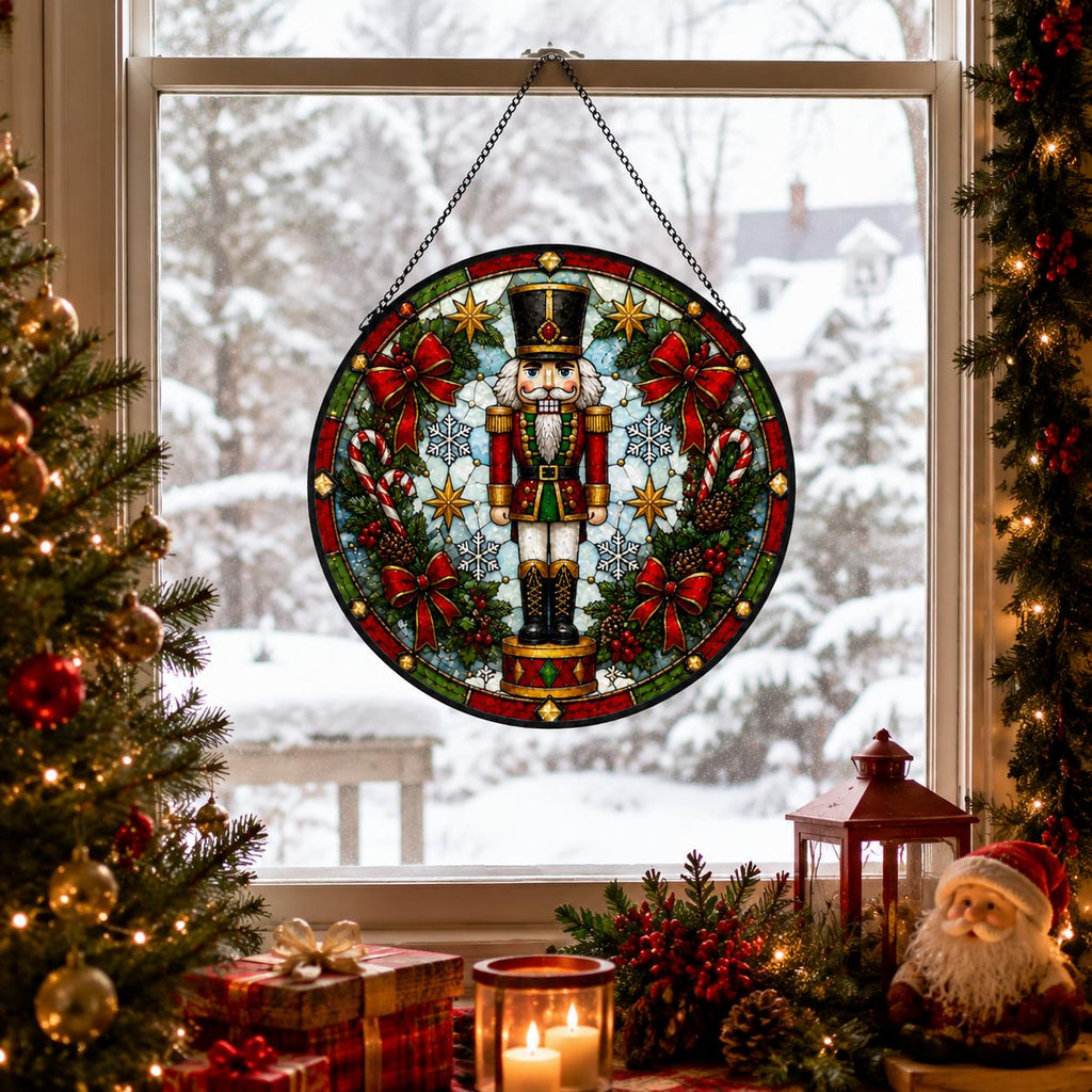 Nutcracker stained glass suncatcher hanging in a snowy Christmas window with tree, candles, lantern, garland and Santa decor.