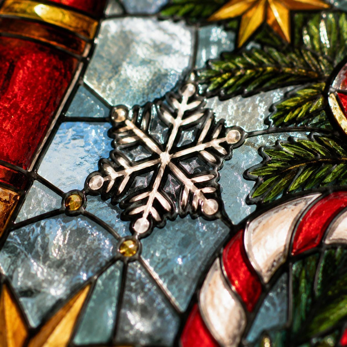 Close-up of nutcracker stained glass suncatcher showing snowflake, candy cane, evergreen branches and textured glass details.