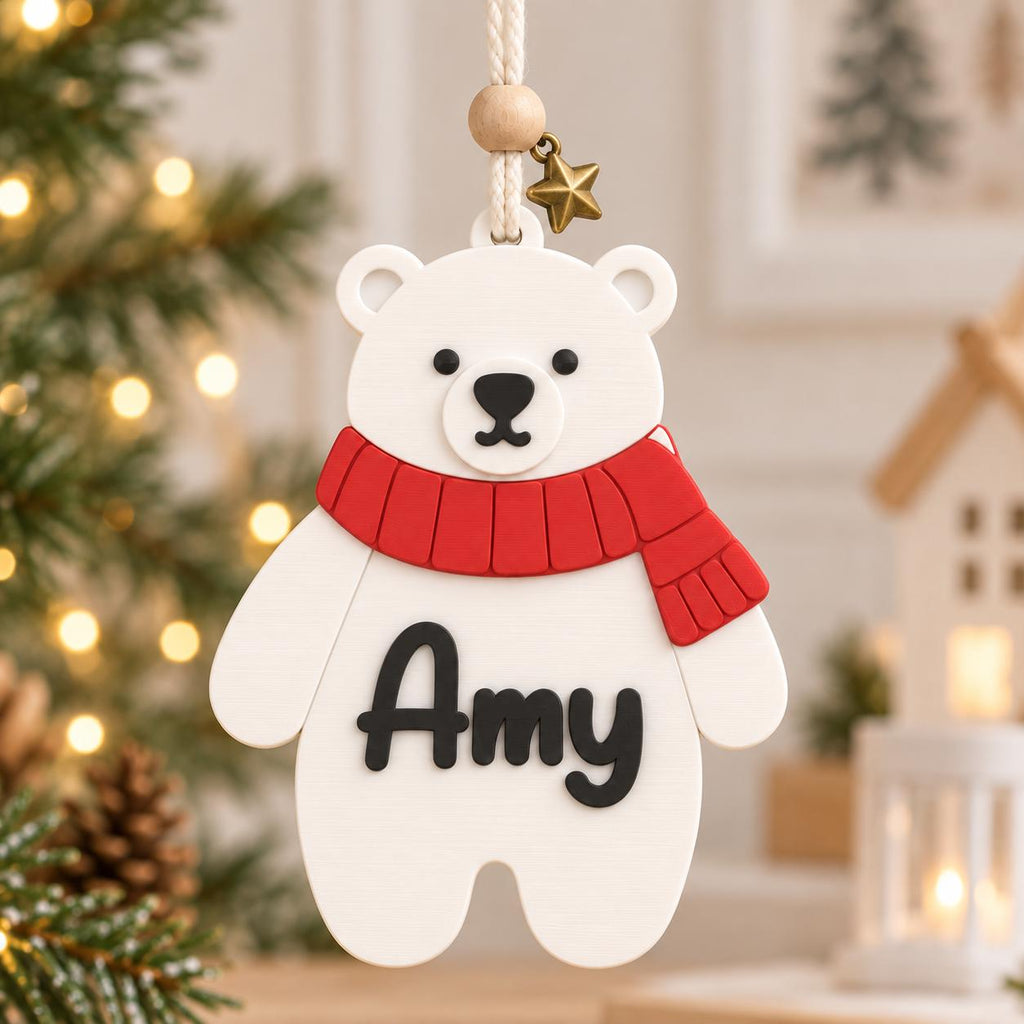May include: A white polar bear ornament featuring a red scarf and the name Amy in black script lettering. The ornament hangs from a white cord with a small wooden bead and a metallic star charm attached at the top of the bear's head.