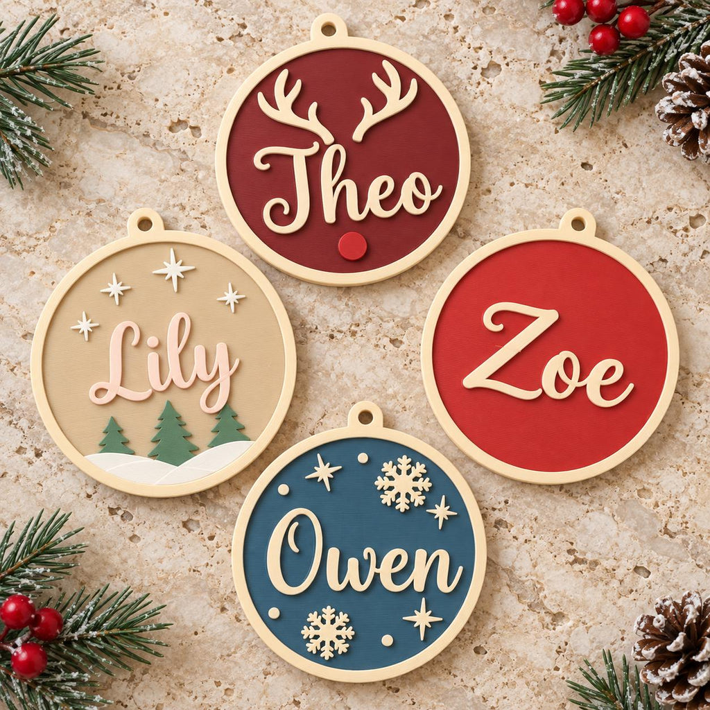 May include: Four circular ornaments with light-colored frames. One is dark red with white antlers and the name Theo. One is beige with white stars, green trees, and the name Lily. One is red with the name Zoe. One is blue with white snowflakes and the name Owen.