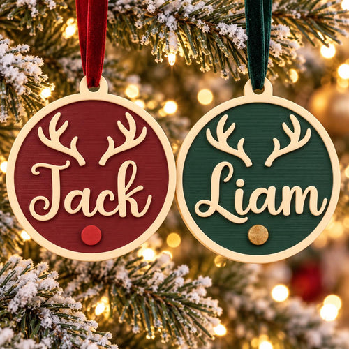 May include: Two circular wooden ornaments with light-colored frames. The left ornament is dark red with the name Jack and cream-colored antlers. The right ornament is dark green with the name Liam and cream-colored antlers. Both have velvet ribbons.
