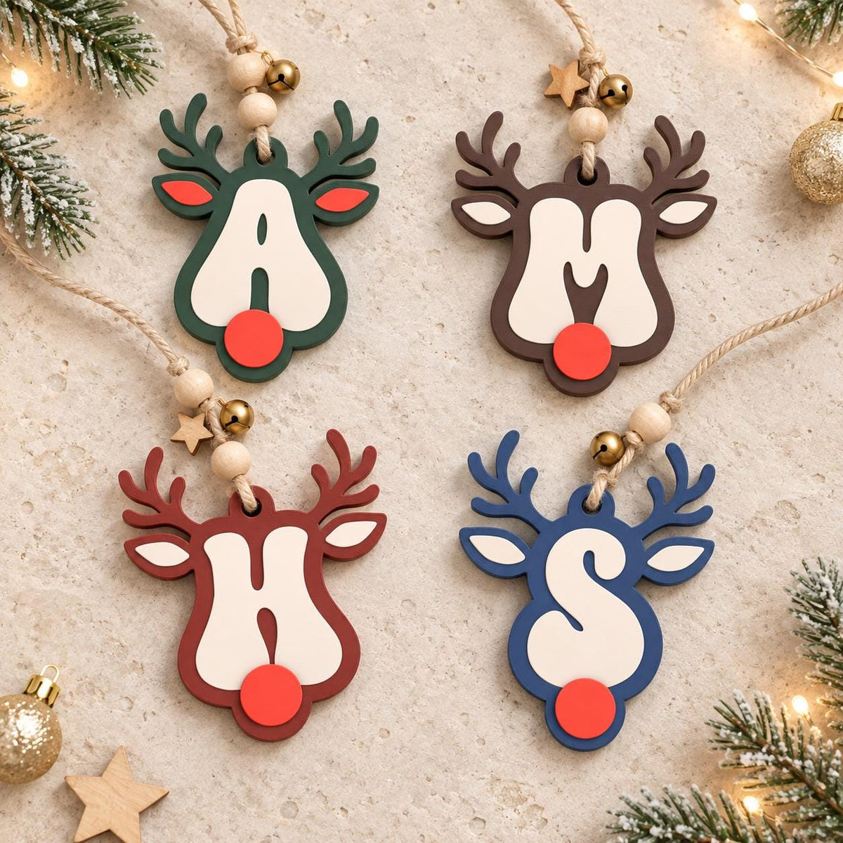 May include: Four hanging ornaments shaped like reindeer heads, each featuring a large cream-colored letter A, M, H, or S in the center. The reindeer have red noses, colored antlers in dark green, brown, red, and blue, and jute twine with wooden beads.