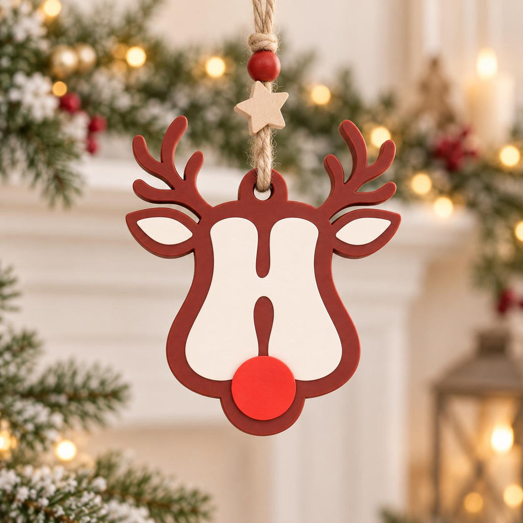 May include: A hanging Christmas ornament shaped like a reindeer head with a dark red outline, a white face, and a bright red circular nose. The ornament is suspended by a jute twine string featuring a small wooden star and a red bead accent.