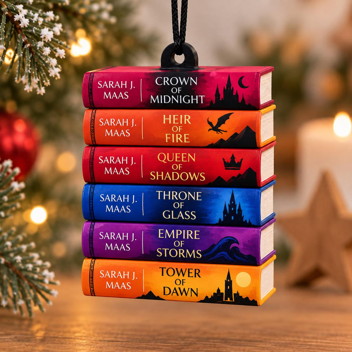 May include: A hanging ornament featuring a stack of six miniature books by Sarah J. Maas, including Crown of Midnight, Heir of Fire, Queen of Shadows, Throne of Glass, Empire of Storms, and Tower of Dawn, with colorful spines and black silhouettes.