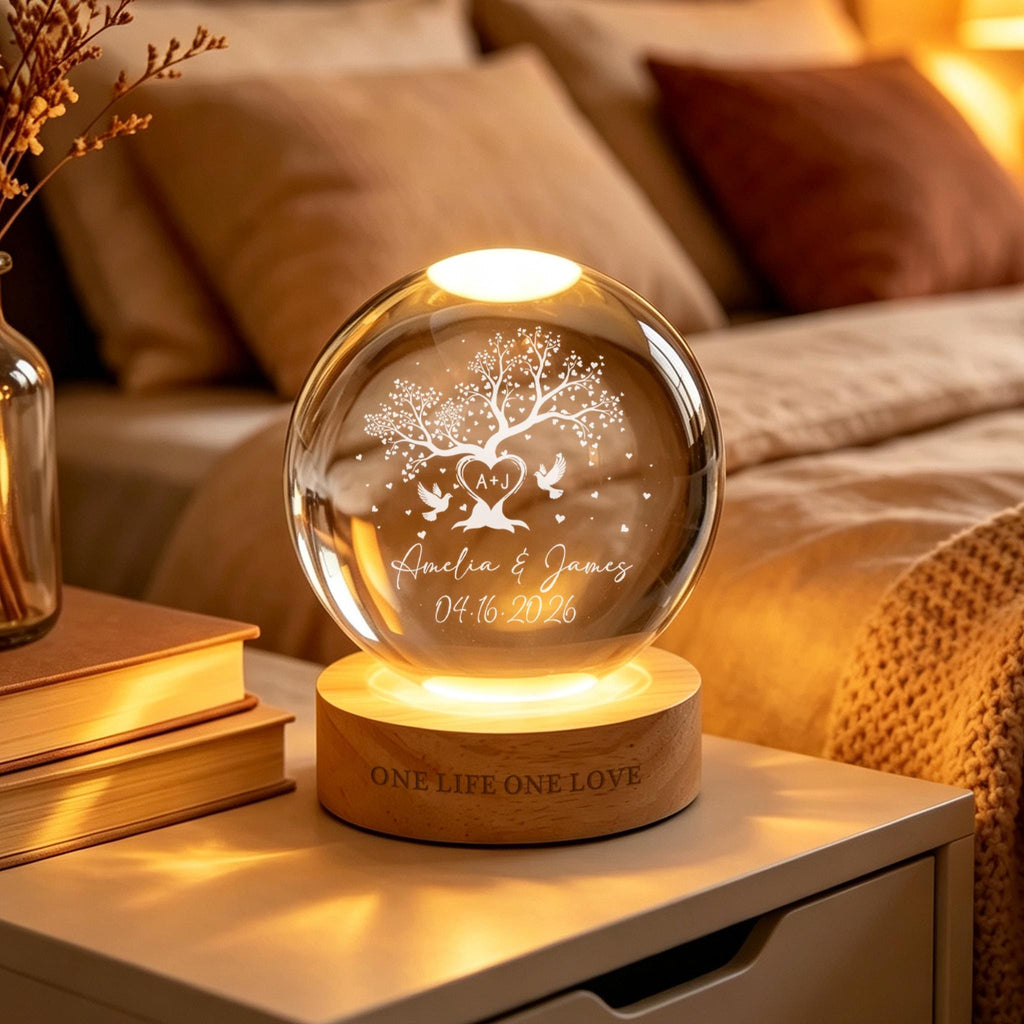 May include: A spherical glass lamp on a round wooden base. The glass features an etched tree, two birds, a heart with the initials A+J, the names Amelia & James, and the date 04.16.2026. The wooden base is engraved with the text ONE LIFE ONE LOVE.