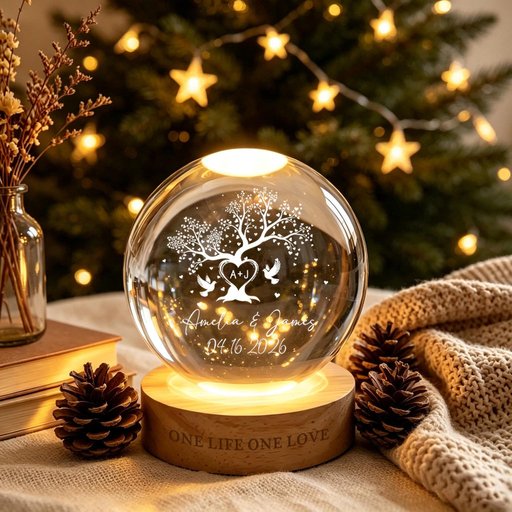 May include: A clear glass sphere lamp on a round wooden base engraved with the text ONE LIFE ONE LOVE. The sphere features an etched design of a tree with heart-shaped leaves, two birds, the initials A+J, and the text Amelia & James 04.16.2026.
