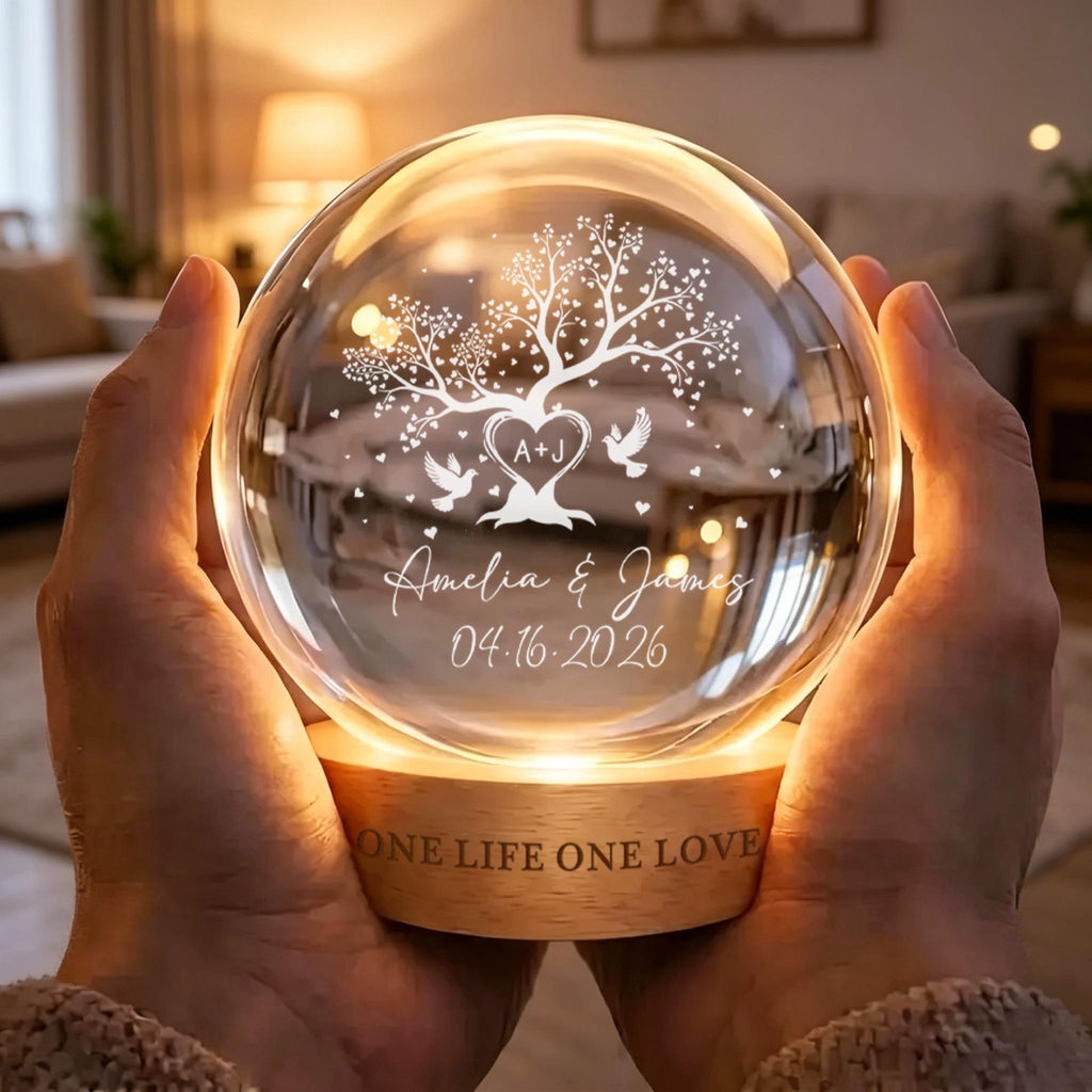 May include: A spherical glass night light on a circular wooden base. The glass features an etched design of a tree with heart-shaped leaves, two doves, and the text A+J, Amelia & James, and 04.16.2026. The wooden base is engraved with ONE LIFE ONE LOVE.