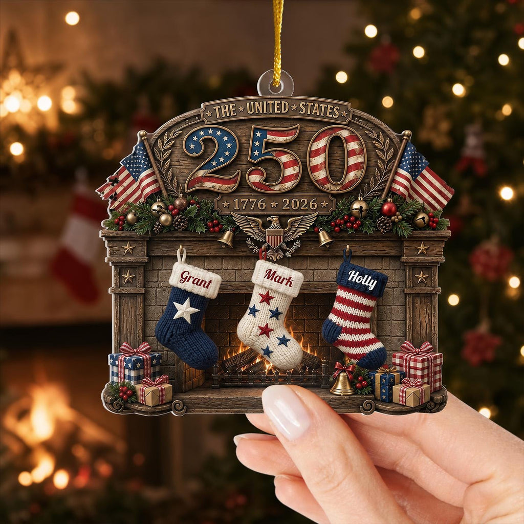 May include: A decorative hanging ornament featuring a fireplace scene with the text THE UNITED STATES 250 and 1776-2026. It includes three stockings labeled Grant, Mark, and Holly, flanked by two American flags, wrapped gifts, and a central eagle emblem.