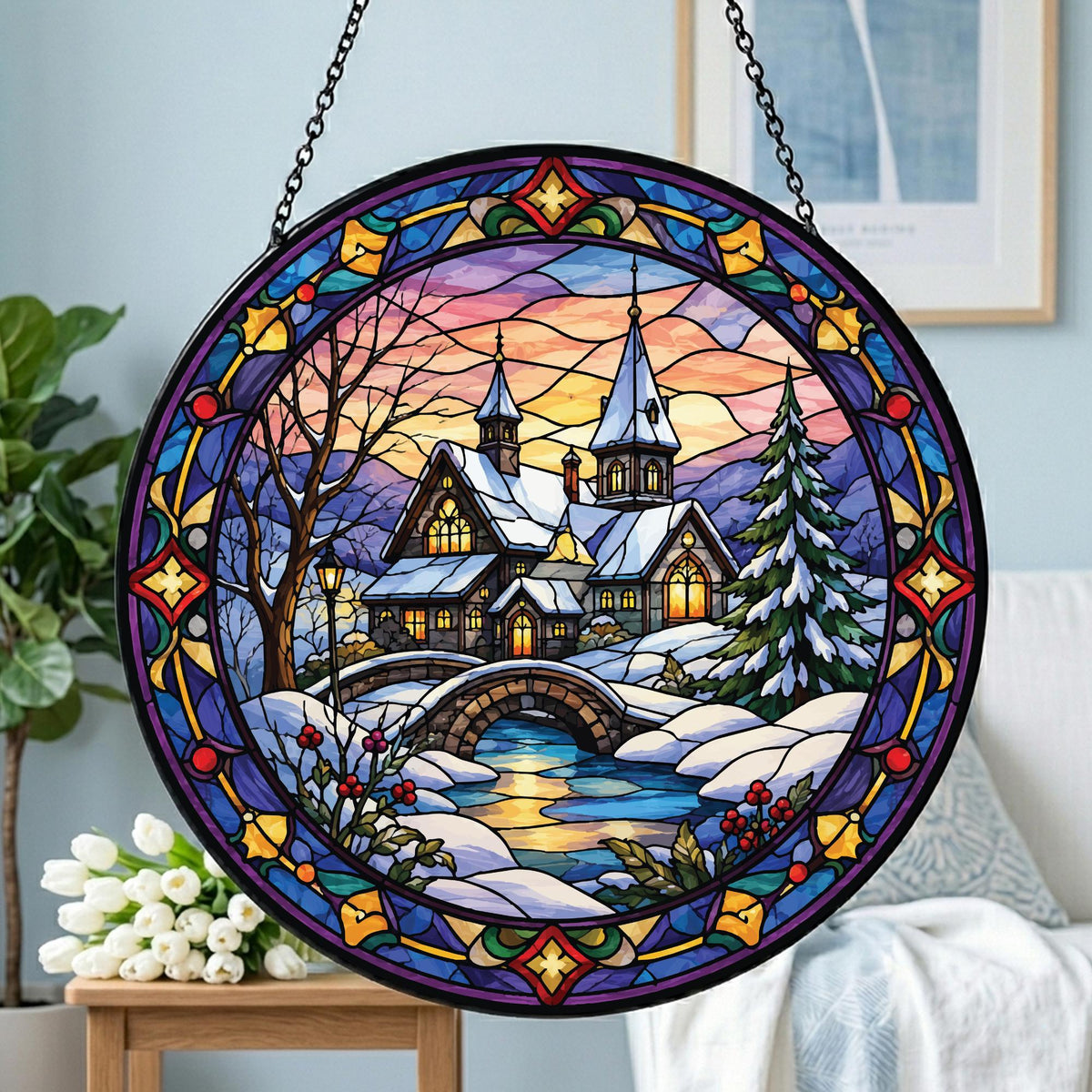 May include: A circular stained glass suncatcher featuring a winter landscape with a snow-covered house, a stone bridge over a stream, and a pine tree. The scene is framed by a decorative border in shades of blue, purple, yellow, and red.